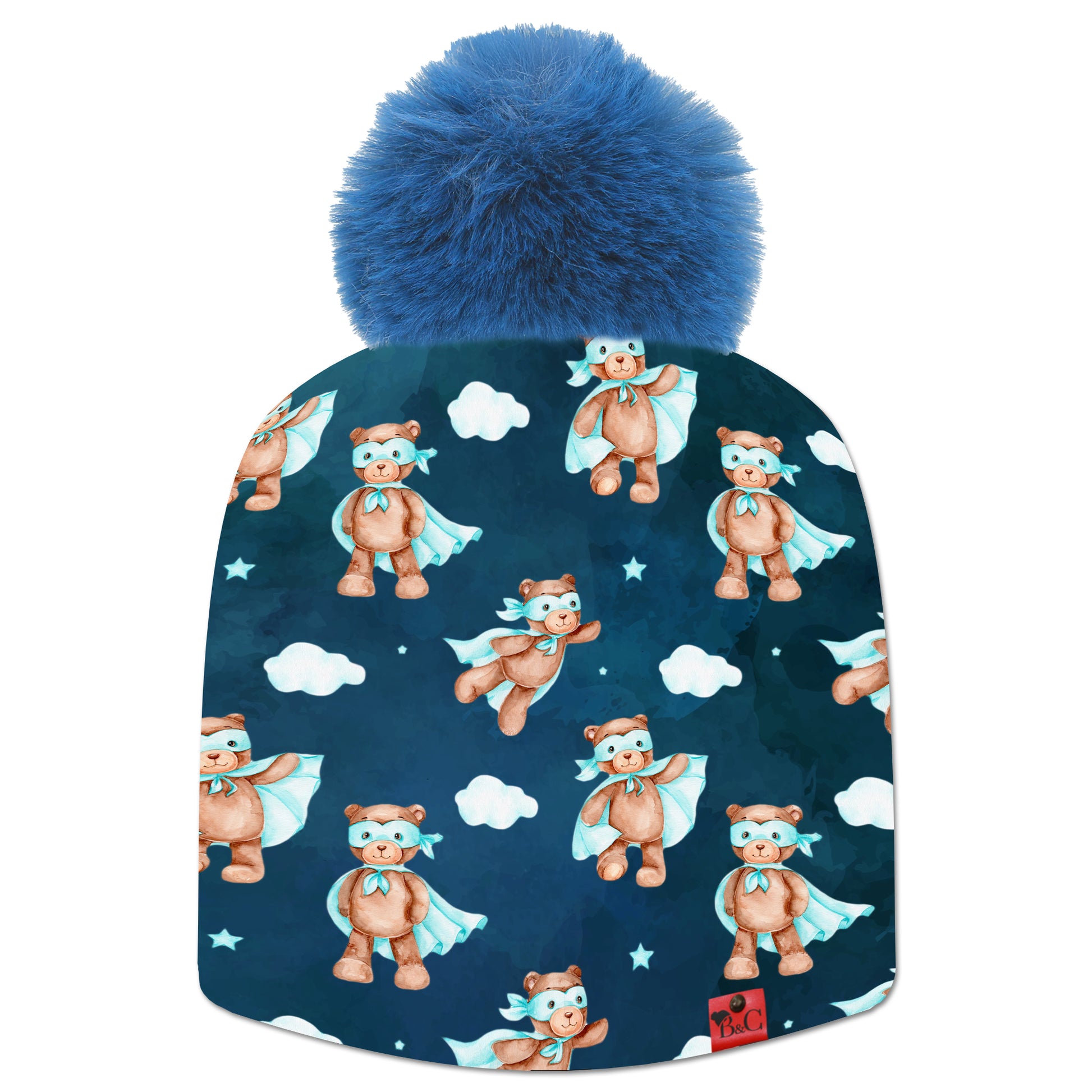 Bonnet Chaplin pour enfants avec un motif d'oursons en costume de super héro bleu ciel, des petitsnuages et un fond bleu foncé. Le bonnet est accompagné de son pompon Indigo en fourrure synthétique et son étiquette en cuir rouge signé Beanie and Clyde.