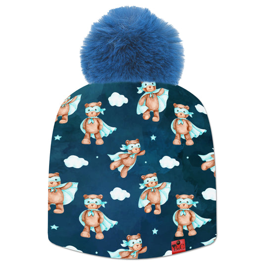 Bonnet Chaplin pour enfants avec un motif d'oursons en costume de super héro bleu ciel, des petitsnuages et un fond bleu foncé. Le bonnet est accompagné de son pompon Indigo en fourrure synthétique et son étiquette en cuir rouge signé Beanie and Clyde.