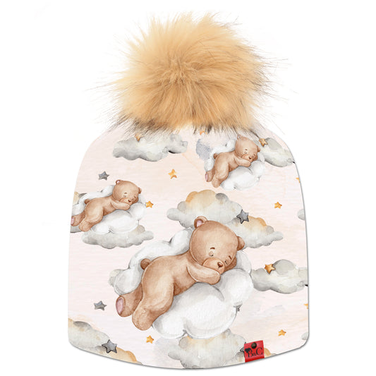 Bonnet Charlie pour enfants, avec un  motif d'ourson qui dort sur un nuage étoilé, accompagné de son pompon Loutre en fourrure synthétique et son étiquette en cuir signé Beanie and Clyde.
