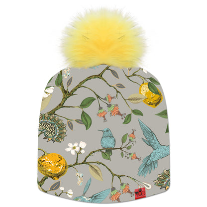 Bonnet Jane pour femmes, un imprimé coloré avec une des oiseaux bleus sur des citroniers. Le bonnet est accompagné de son pompon Citron en synthétique et de son étiquette en cuir rouge signée Beanie and Clyde.