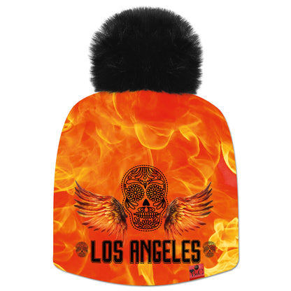 Bonnet Marilyn pour hommes et femmes avec une tête de mort, des ailes sur un fond orangé en flamme et l'inscription "Los Angeles" et son pompon en fourrure synthétique noir. Avec son étiquette en cuir rouge signée Beanie and Clyde vous ne passerez pas inaperçu, de quoi apporter une touche audacieuse à votre tenue.