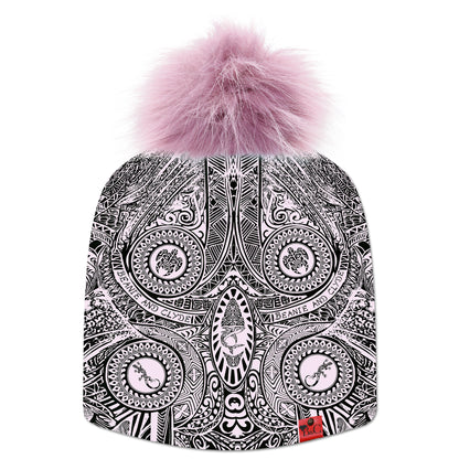 Bonnet Moana pour enfants, décoré de motifs d’inspiration maorie et polynésienne en rose pâle et noir. Il est surmonté d’un pompon Pourpre en fourrure synthétique, et orné de la signature en cuir rouge de Beanie & Clyde.