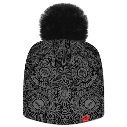 Bonnet Roa pour hommes et femmes, orné de motifs d’inspiration maorie et polynésienne en négatif, rendu en nuances de gris, Il est surmonté d’un pompon Noir en fourrure synthétique, et rehaussé par l’étiquette en cuir rouge emblématique de Beanie & Clyde.